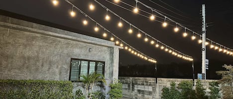 A building with a concrete facade, a window with shutters, and a series of string lights.