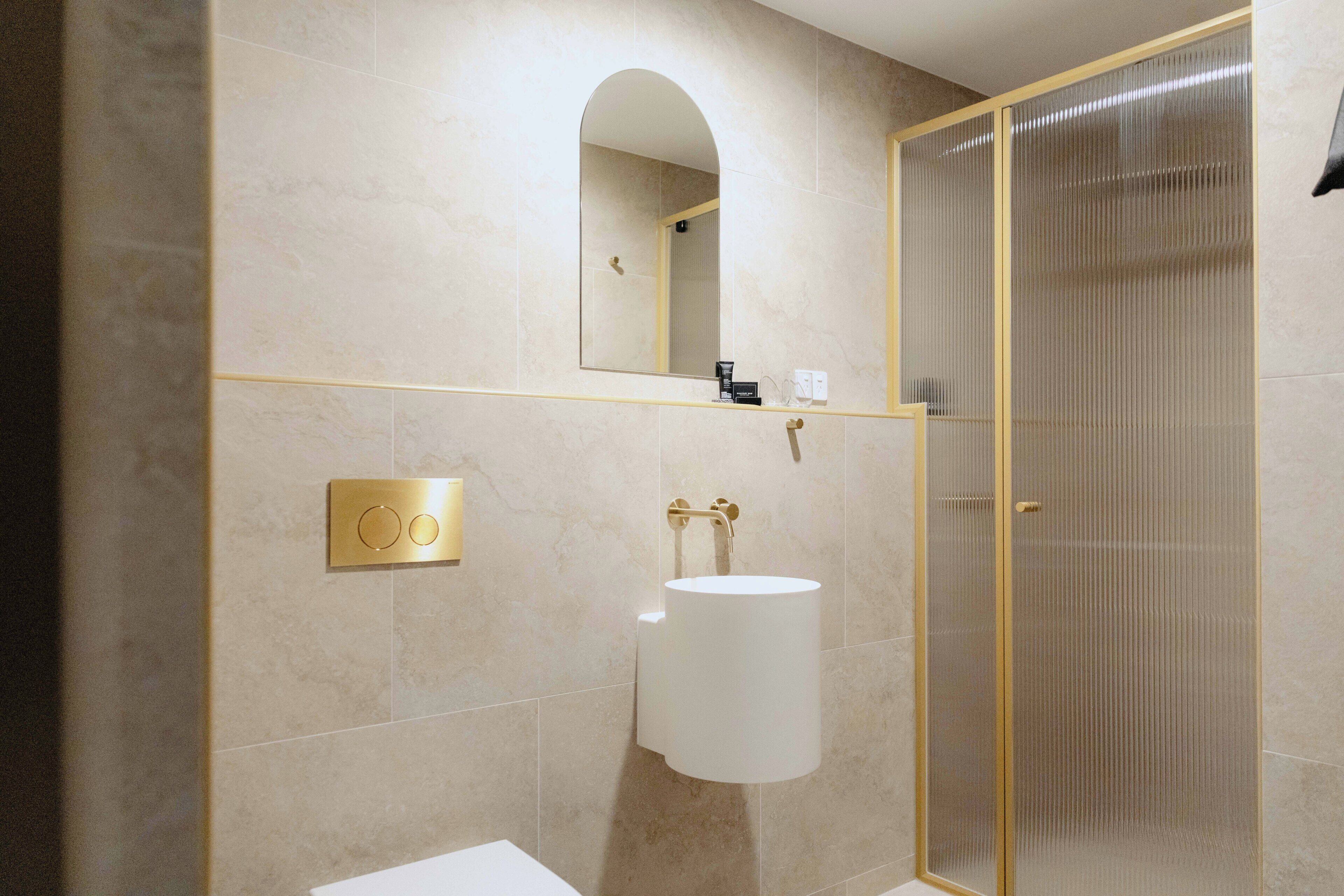 Une salle de bain avec un lavabo blanc, un miroir à cadre doré et une cabine de douche dotée d’une porte en verre.