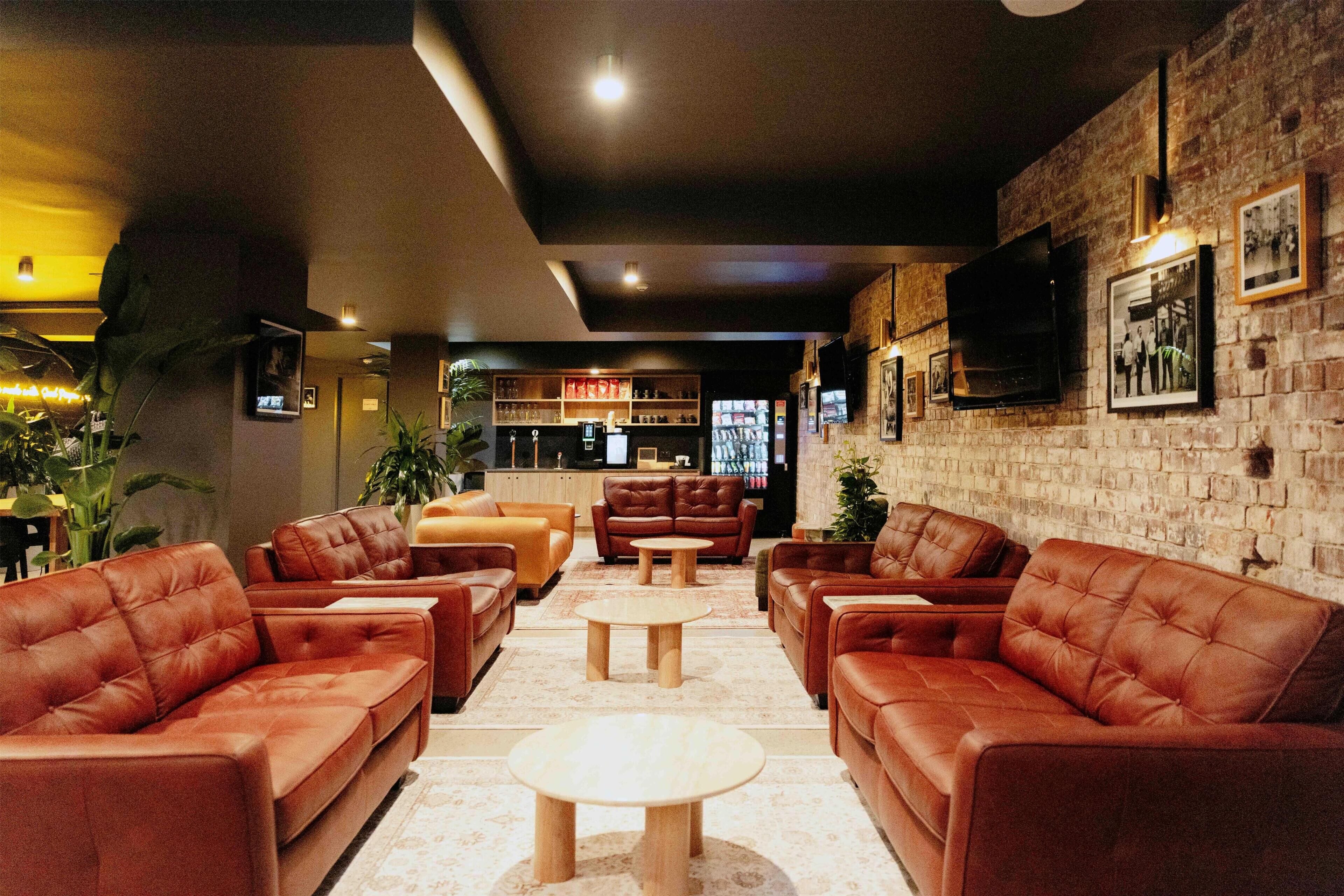 A lounge area with leather sofas, a coffee table, and a brick wall with framed pictures.