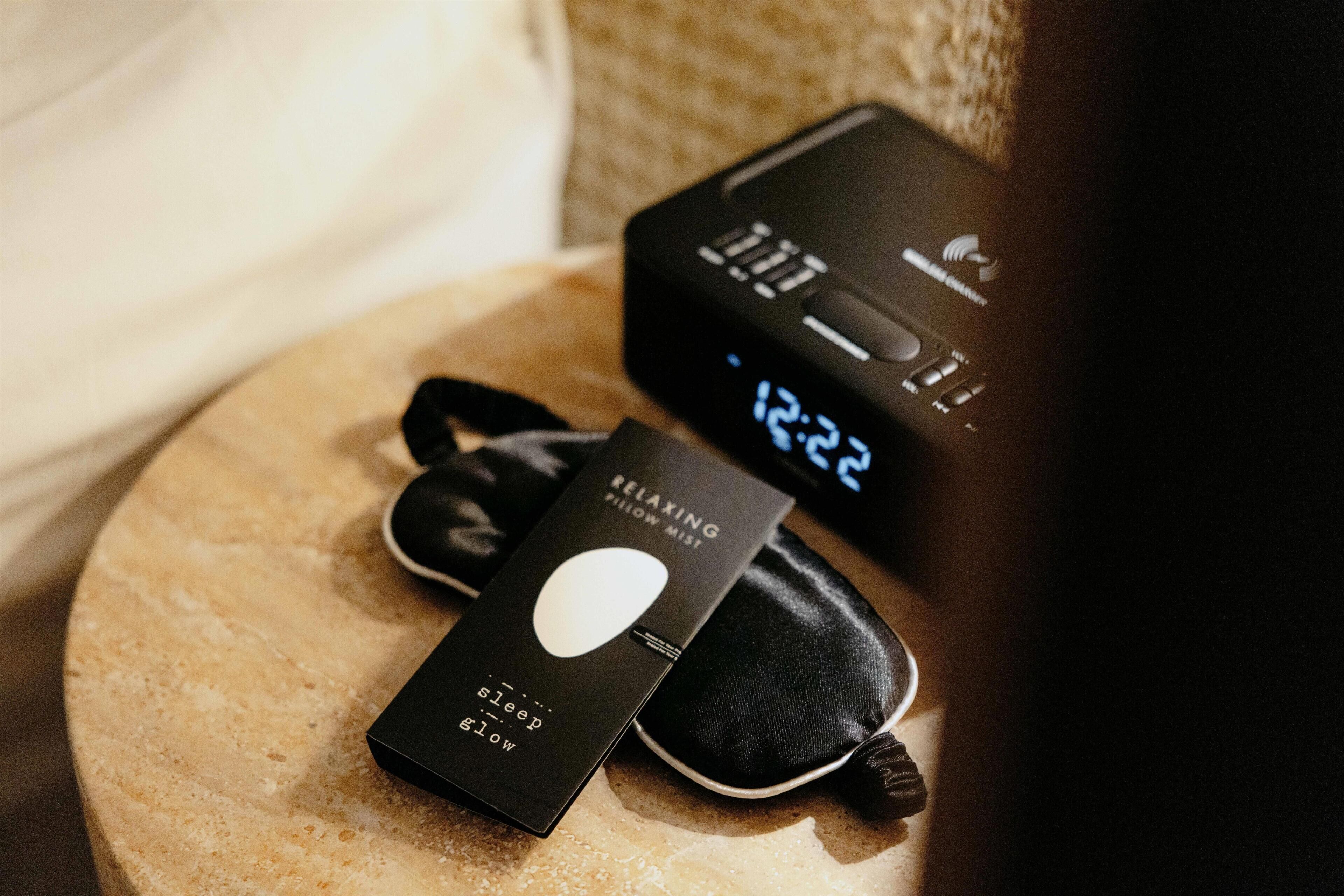 A pillow, a remote control, and a digital clock on a surface.