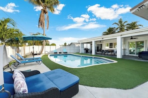 A backyard with a swimming pool, artificial grass, lounge chairs, and a covered patio area. - Ivory House- Private Retreat with Pool Near Beach (Hollywood)