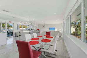 A modern hotel dining area with a glass table, red placemats, white chairs, and a view of the outdoors. - Ivory House- Private Retreat with Pool Near Beach (Hollywood)