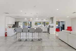 A modern kitchen with white cabinets, a central island with bar stools, and an exit sign. - Ivory House- Private Retreat with Pool Near Beach (Hollywood)