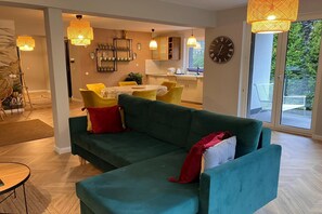 A modern living room with a teal sofa, yellow chairs, and a dining area with a round table.