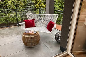 A white wicker chair with red cushions on a balcony with a view of trees. - Comfortable Jacuzzi Apartment for 8 in Stezyca (Stezyca)