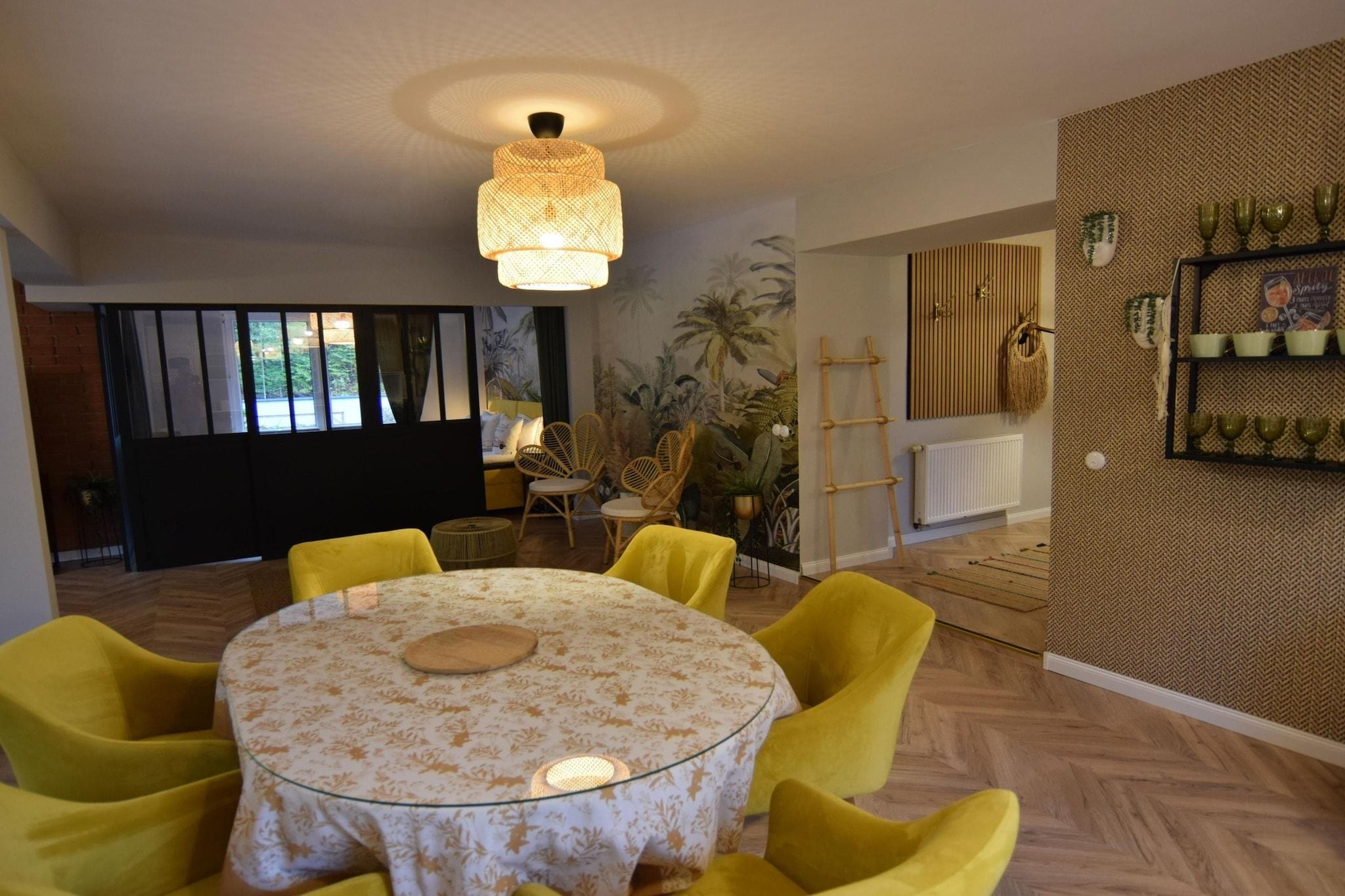 Un espace repas avec une table ronde, des chaises jaunes, un luminaire suspendu et un mur orné d’un motif en chevrons.