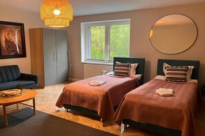 A hotel room with two beds, a sofa, a dining table, a large window, and a hanging light fixture.