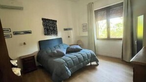 Une chambre à coucher comprenant un lit, une table de chevet, une commode, une fenêtre avec des rideaux et un luminaire au plafond.