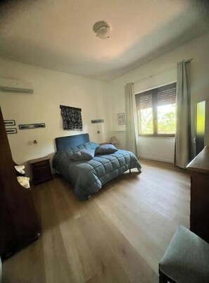 Une chambre à coucher comprenant un lit, une table de chevet, une commode, une fenêtre avec des rideaux et un luminaire au plafond.
