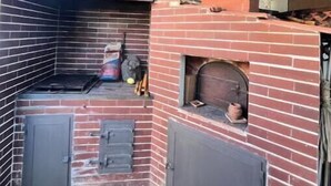 Un four en briques doté d’une hotte métallique, d’une petite étagère et d’une porte.