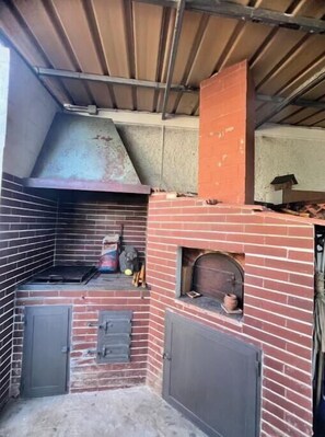 A brick oven with a metal hood, a small shelf, and a door.