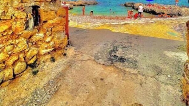 Un bâtiment en pierre avec une enseigne indiquant « Baglio Carini » et une vue sur la mer.