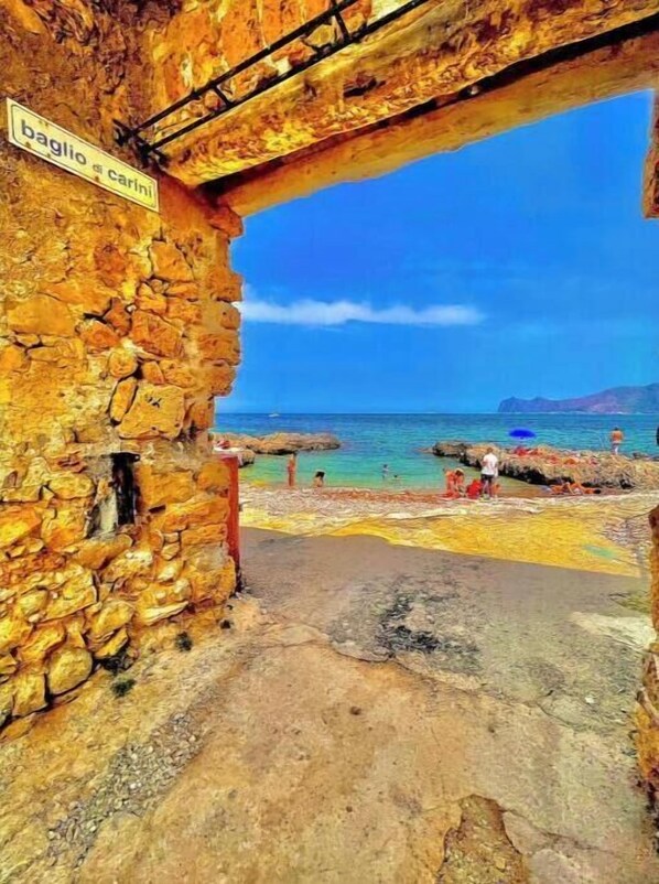 Un bâtiment en pierre avec une enseigne indiquant « Baglio Carini » et une vue sur la mer.