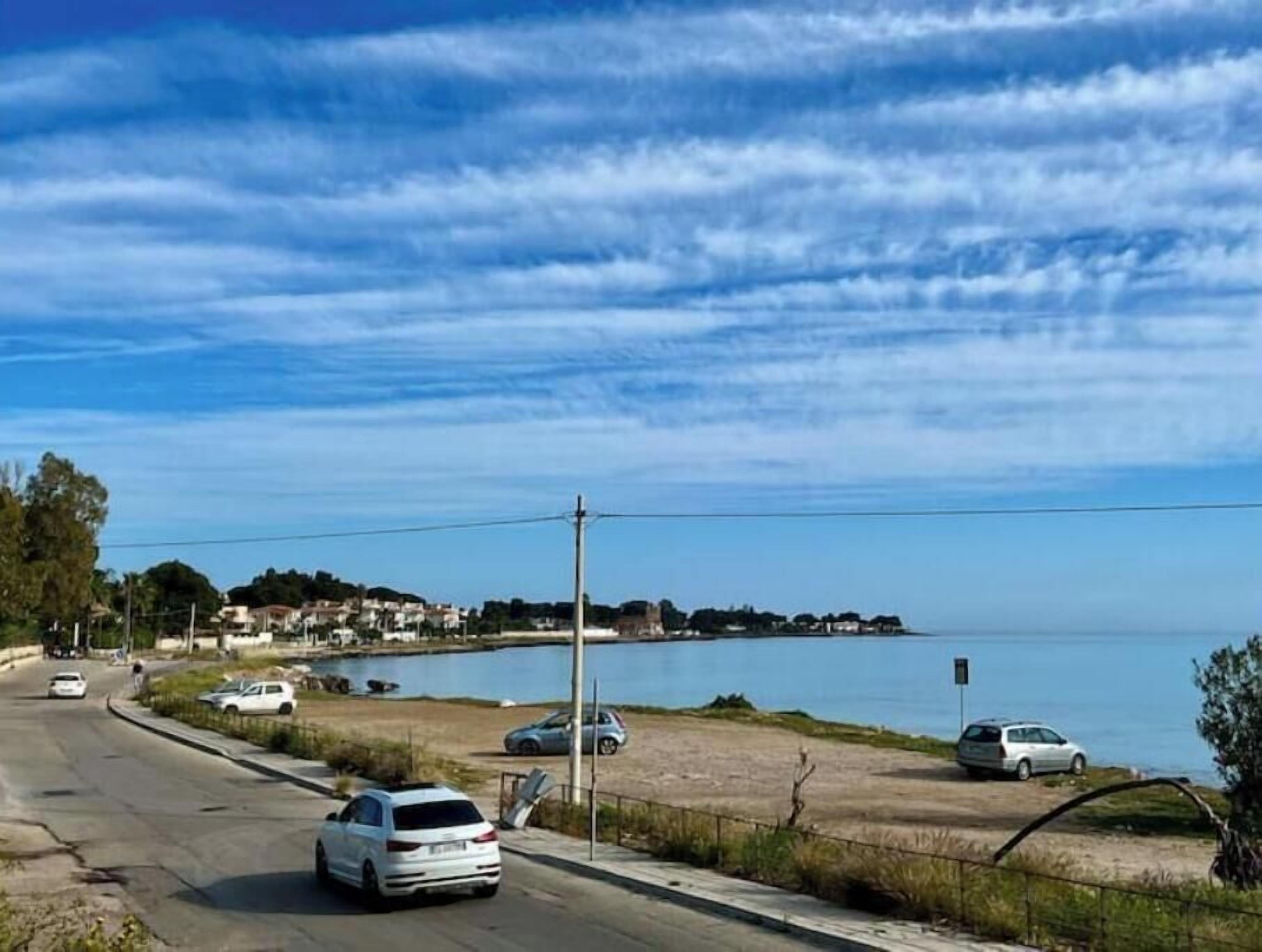 A coastal road with cars, a clear sky, and a distant shoreline.