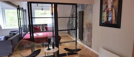 A modern room with a glass partition, a sofa, a red rug, and a framed picture on the wall.