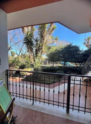 A balcony with a metal railing, a tiled floor, and a view of trees and a building in the background. - Lulu House - Mandarins (Carini)