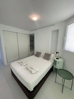 Ein modernes Schlafzimmer mit einem großen Bett, einem Nachttisch, einem grünen Sessel und einem Kleiderschrank.