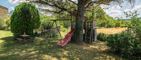 A playground with a slide and climbing structures, surrounded by trees and grass.
