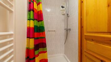 Un espace douche avec un mur recouvert de carreaux blancs, une pomme de douche et un rideau de douche rayé et coloré.