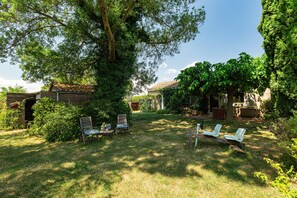 Un jardín con un banco de madera, una mesa pequeña y un árbol.