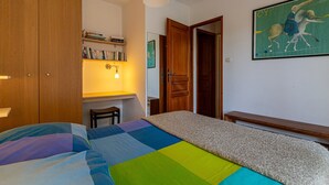 Una camera da letto con un letto, un armadio in legno, una libreria, una scrivania e un quadro appeso al muro.