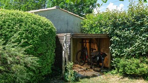 Un piccolo capanno con una bicicletta all'interno, immerso nel verde.