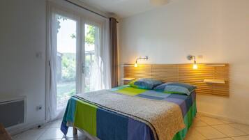 Une chambre à coucher avec un lit, une fenêtre avec des rideaux, un radiateur et deux lampes fixées au mur.