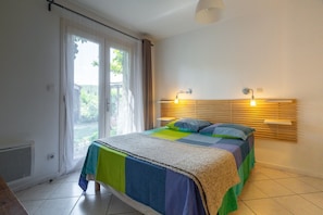 Un dormitorio con una cama, un ventanal con cortinas, un radiador y dos lámparas de pared.