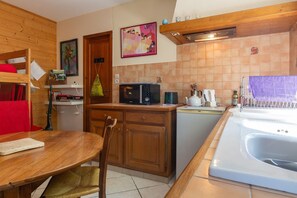 Cocina compacta con armarios de madera, microondas, hervidor y pileta.