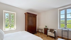 Un dormitorio con cama, armario, radiador, silla, mesa y ventana con vistas.