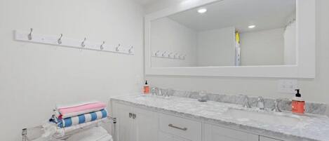 Un baño con un espejo grande, muebles blancos, un perchero y una encimera de mármol.
