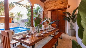 A dining area with a pool view, wooden tables, and tropical plants. - 5-Star Getsemani Villa | Private Pool | Sleeps 18 (Cartagena de Indias)