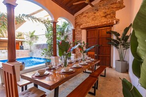 A dining area with a pool view, wooden tables, and tropical plants. - 5-Star Getsemani Villa | Private Pool | Sleeps 18 (Cartagena de Indias)