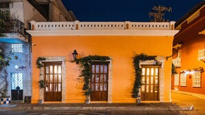 A building with three wooden doors and windows, a white balcony, and a street view. - 5-Star Getsemani Villa | Private Pool | Sleeps 18 (Cartagena de Indias)