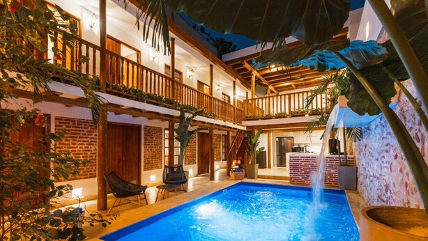 A pool area with a wooden deck, lounge chairs, and a water feature. - 5-Star Getsemani Villa | Private Pool | Sleeps 18 (Cartagena de Indias)