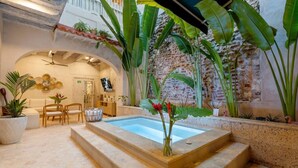 Ein Poolbereich mit Steinrand, Zimmerpflanzen und einer Sitzgelegenheit mit Stühlen und einem Tisch.
