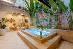 Un'area piscina con bordo in pietra, piante da interno e un angolo relax con sedie e tavolo.