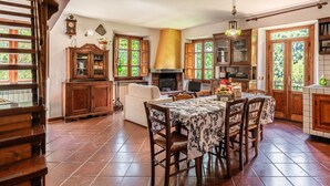 A kitchen with wooden cabinets, a dining table with chairs, a fireplace, and large windows. - Apartment in Villa Poesia - Bagni di Lucca (Bagni di Lucca)