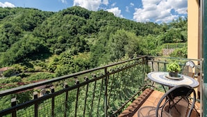 A balcony with a table and chairs, overlooking a lush green hillside. - Apartment in Villa Poesia - Bagni di Lucca (Bagni di Lucca)