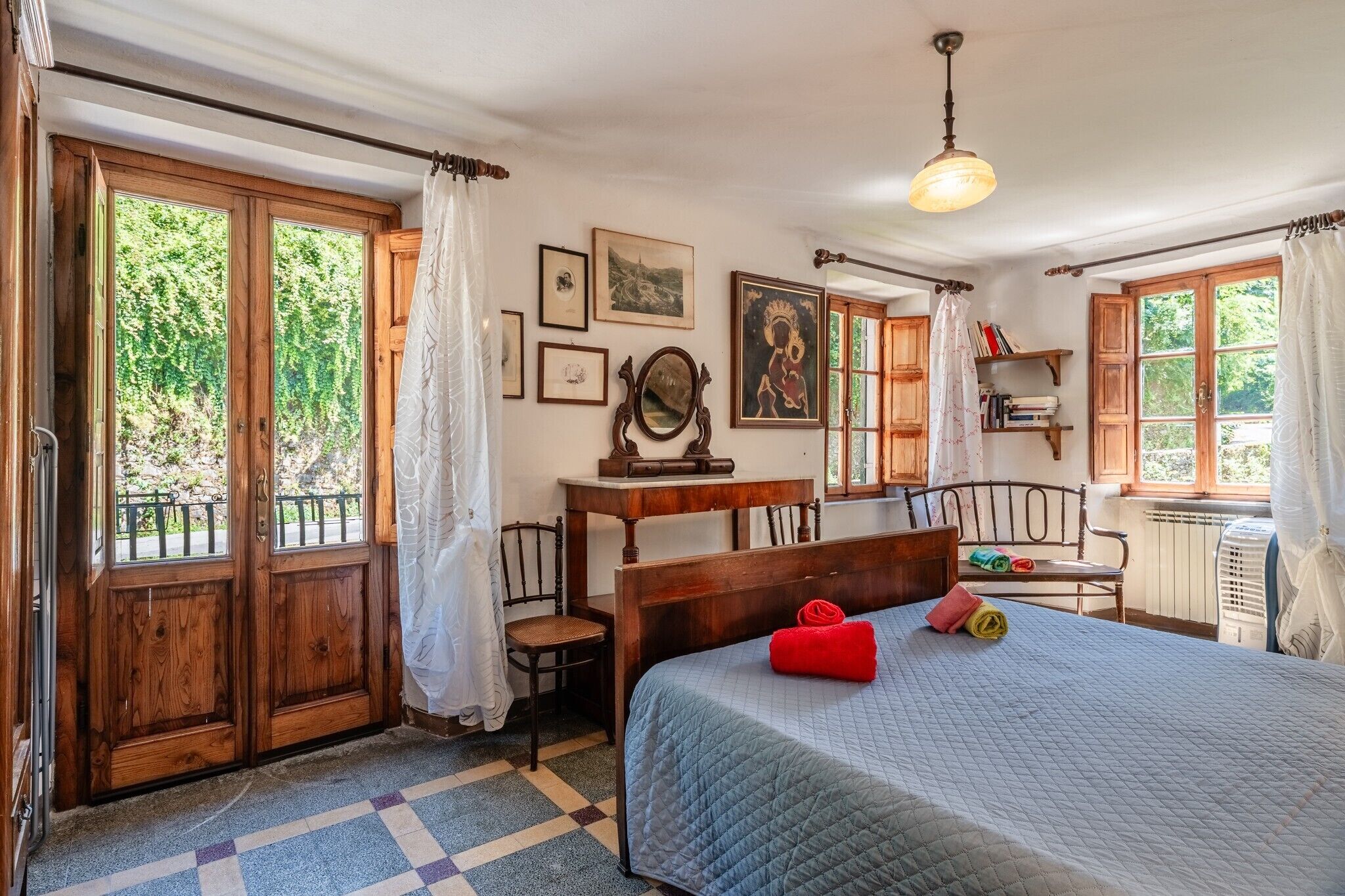 A bedroom with a bed, a desk, a chair, a radiator, and a window with curtains.