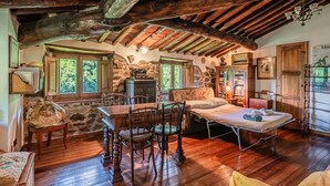 A rustic room with a wooden table, chairs, a bed, and a stone wall. - Apartment in Villa Poesia - Bagni di Lucca (Bagni di Lucca)