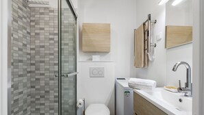 Een moderne badkamer met een douchecabine van glas, een toilet, een wastafel met een handdoek en een spiegel.