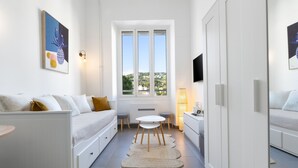Een smalle kamer met een bed, een klein tafeltje, een stoel, een raam met uitzicht en een aan de muur bevestigde televisie.