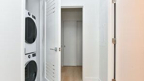 A laundry room with two washing machines and a door leading to a hallway. - Urban Escape : Bright 2BR/2BA in FiDi (New York)