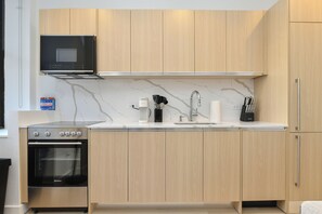 A modern kitchen with wooden cabinets, a built-in microwave, a stainless steel oven, and a white countertop. - Urban Escape : Bright 2BR/2BA in FiDi (New York)