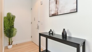 A hallway with a potted plant, a black console table with two vases, and a painting on the wall. - Urban Escape : Bright 2BR/2BA in FiDi (New York)
