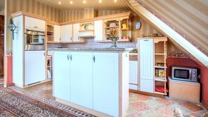Una cocina con armarios blancos, horno empotrado, microondas y refrigerador pequeño.