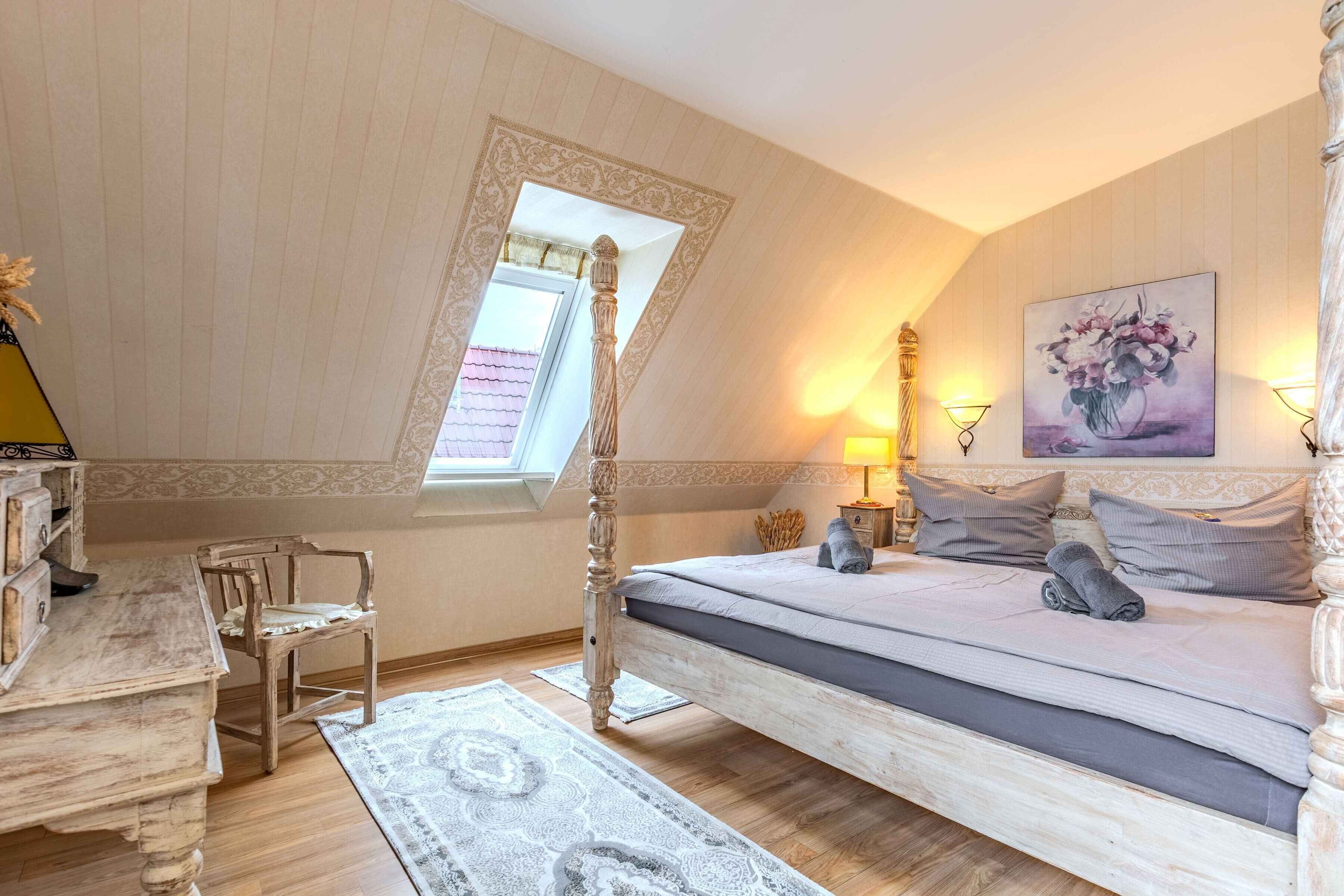 A bedroom with a wooden bed, a desk, a chair, a window, and a painting on the wall.