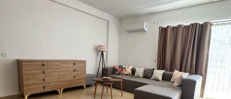 Un salon moderne avec un canapé, une commode en bois, une lampe et un luminaire suspendu.