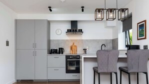 A modern kitchen with grey cabinets, a built-in oven, a coffee machine, and two bar stools. - Spacious 2BR - Parking Near Edinburgh City Centre (Edinburgh)